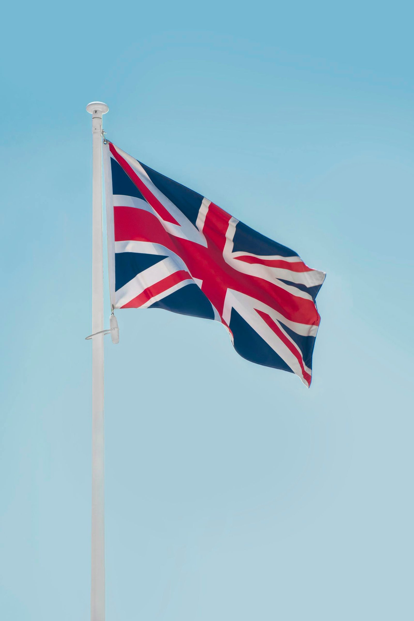 Union Jack flag waving on a flagpole against a clear blue sky in London.